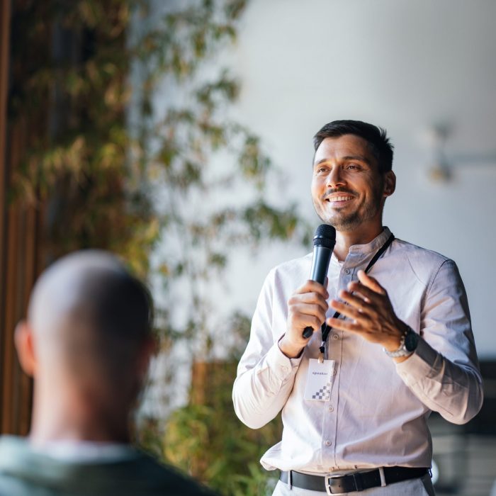 A man holding a microphone confidently speaking and engaging an audience at a business event