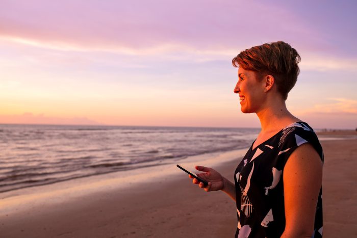 Person holding a phone on a beach during sunset.
